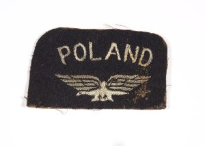 Onto a rectangular patch of black melton with rounded upper corners, POLAND above an eagle all embroidered in pale gold thread.