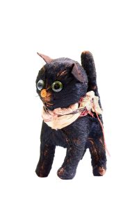 Small black toy cat, made of cotton with wool wadding, fur-fabric, and green glass eyes. Fur worn bare in places. White silk collar.
