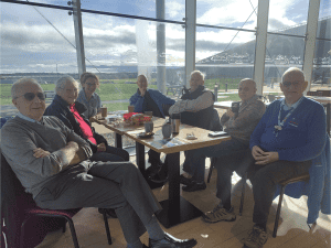 A group of carers and RAF Museum volunteers sit round a table with coffee and biscuits.