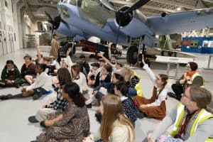 Children sitting among aircraft putting hand up