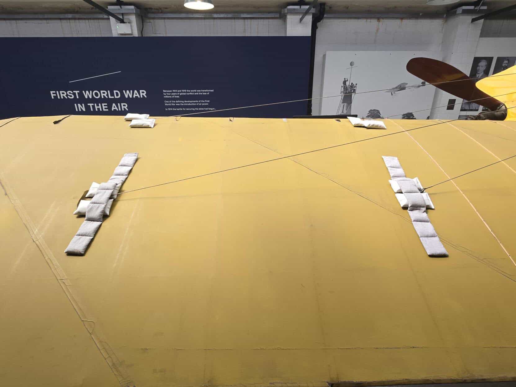 Close-up of the Blériot XXVII during conservation treatment, showing temporary support weights used to stabilise and reshape the historic wing covering.